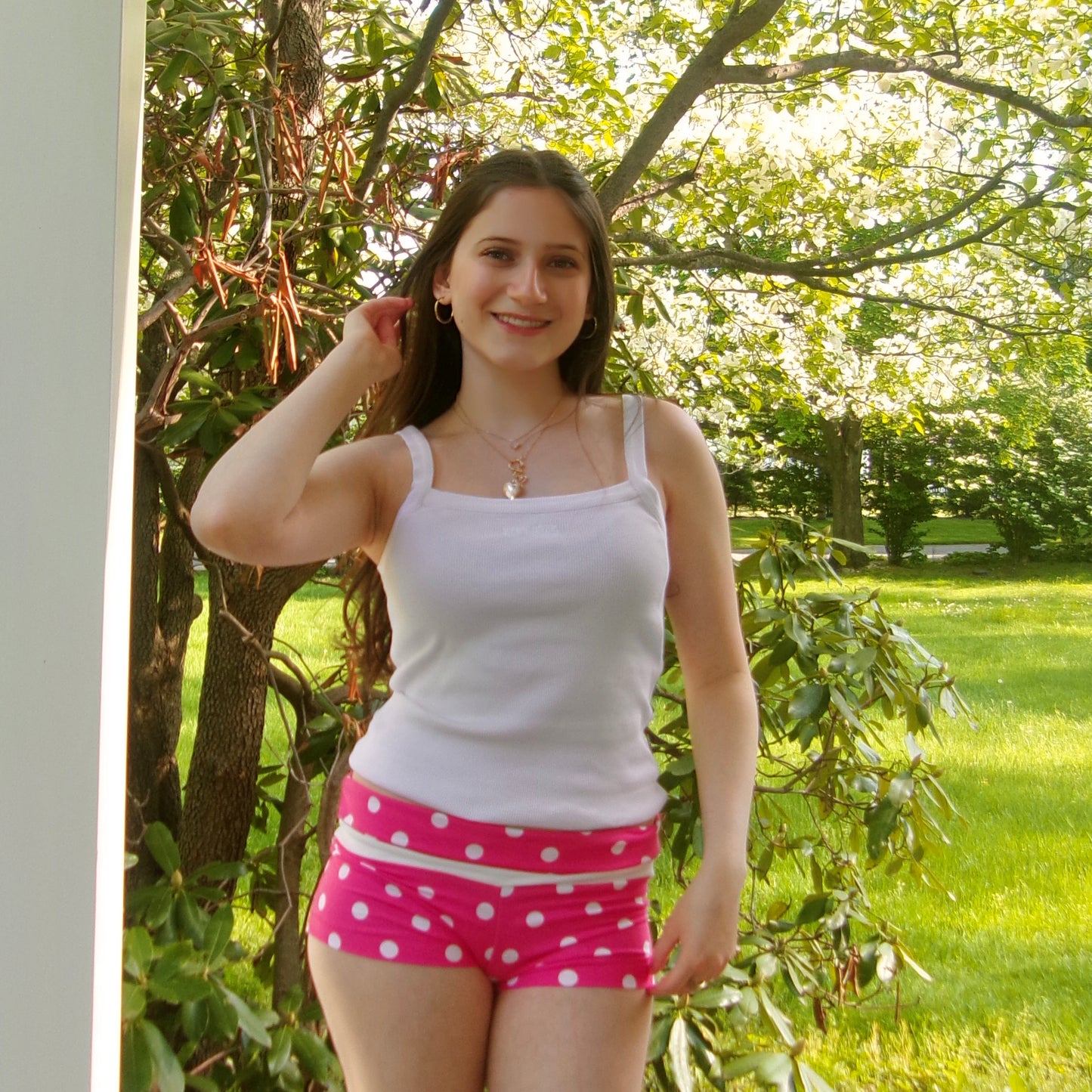 Model wearing micro pink and white polka dot shorts with a fold-over waistband, standing straight.