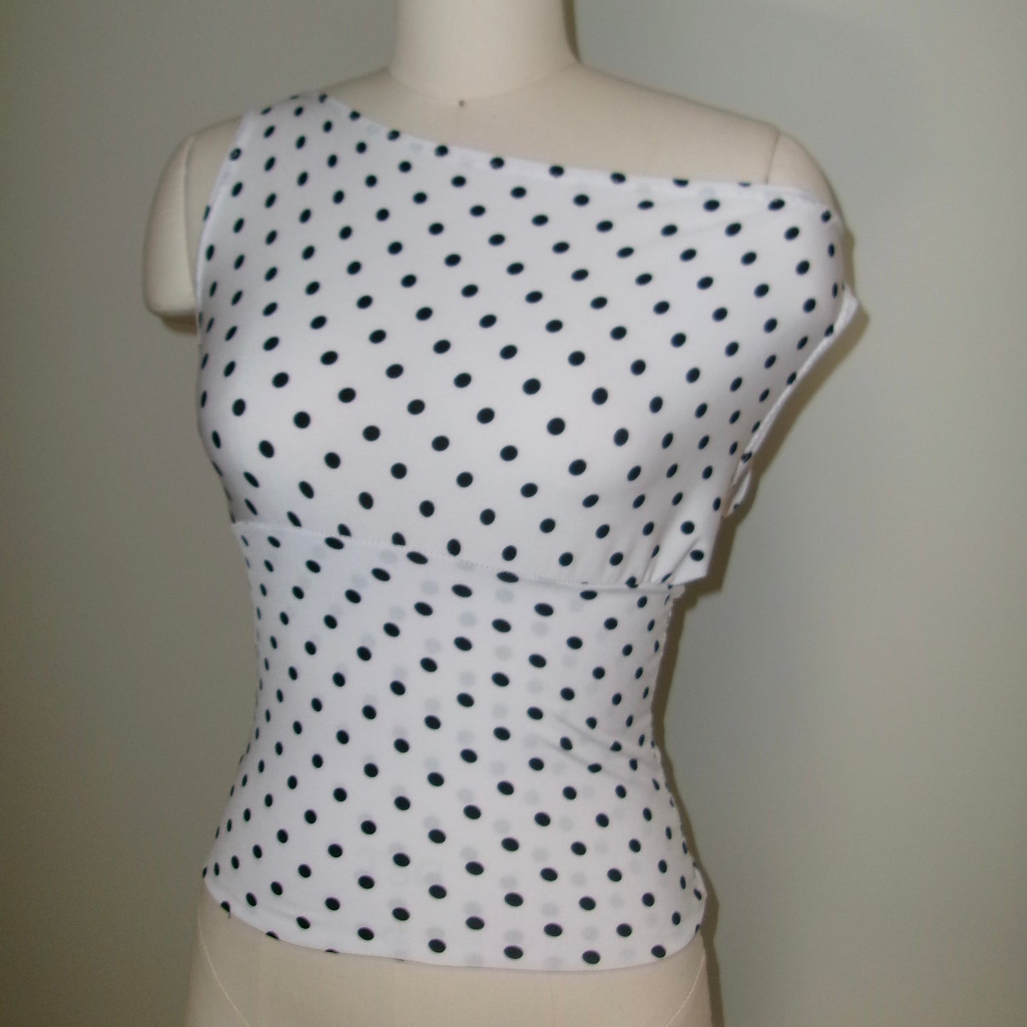 White sleeveless top with black polka dots on a mannequin against a plain background