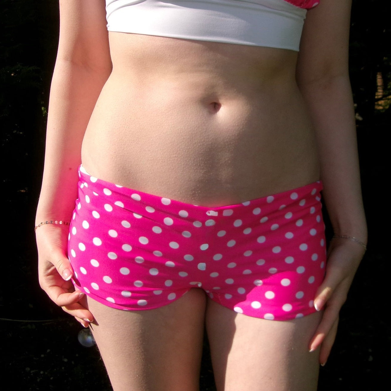 Person wearing pink polka dot shorts with a white top against a dark background
