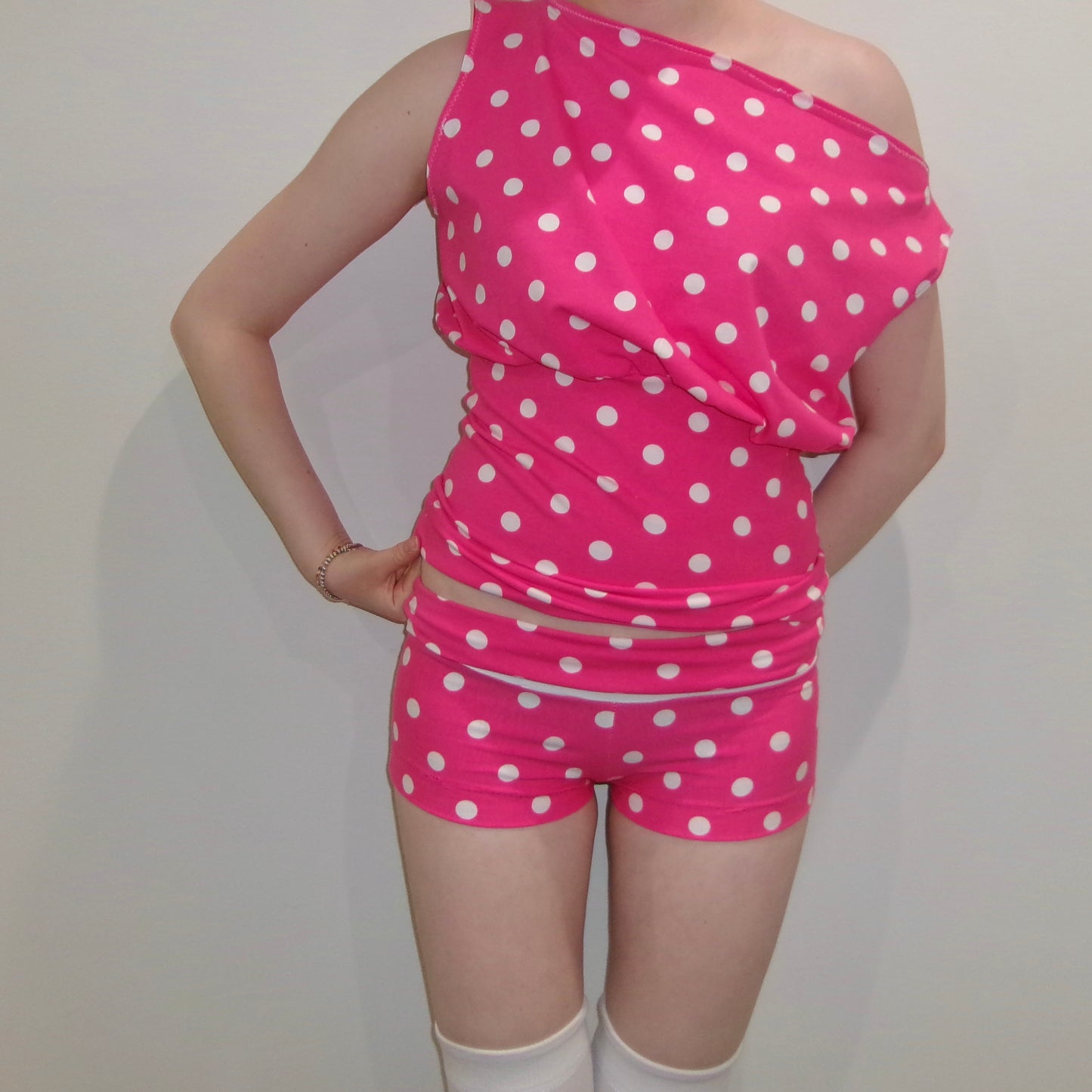 Model wearing a pink and white polka dot off-shoulder tank top. Standing in soft lighting. Retro, trendy, Y2K, preppy, chic