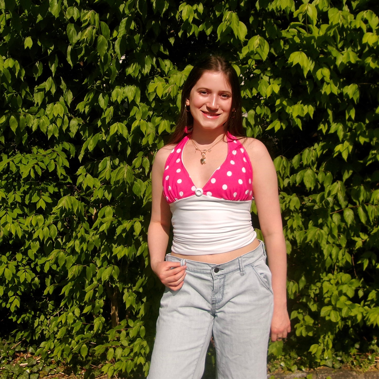 Model wearing a pink and white polka dot halter top with a tie-neck and fitted bodice, standing in natural sunlight.