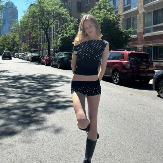 Woman in black polka dot outfit walking on a city street.