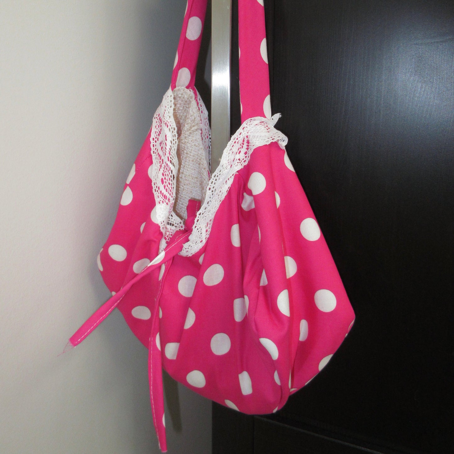 Pink polka dot bag with lace trim hanging on a dark surface.