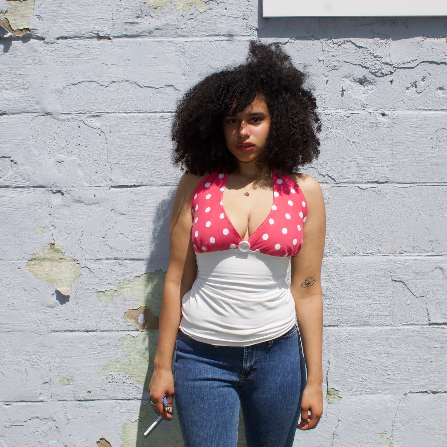 Woman wearing a pink polka dot top over a white shirt against a textured wall.