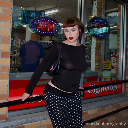 Woman posing in front of a store with neon signs, including an ATM sign.