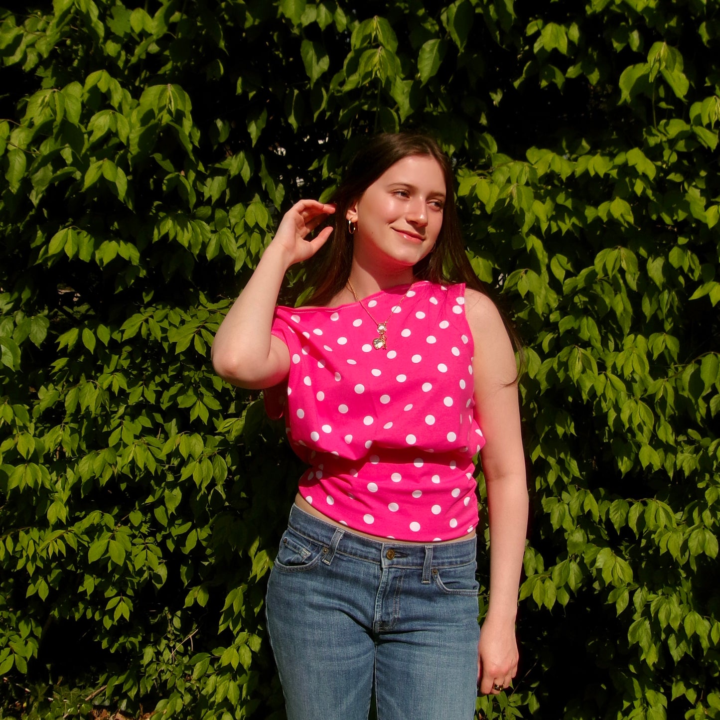Model wearing a pink and white polka dot off-shoulder tank top. Standing in soft lighting. Retro, trendy, Y2K, preppy, chic