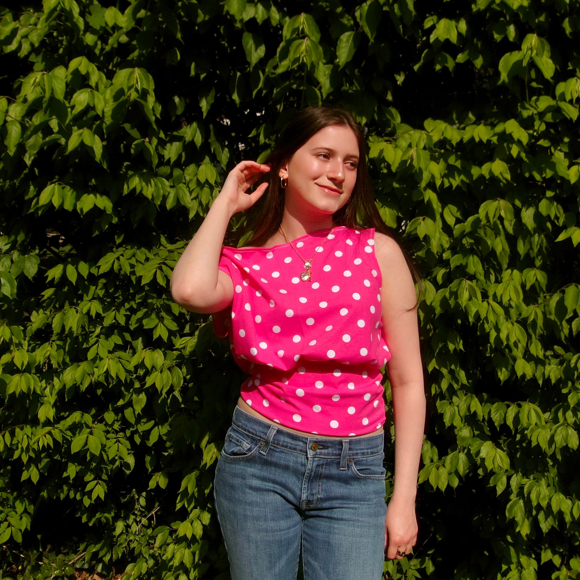 Model wearing a pink and white polka dot off-shoulder tank top. Standing in soft lighting. Retro, trendy, Y2K, preppy, chic
