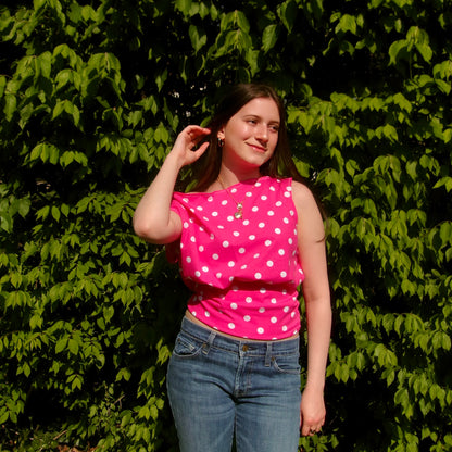 Model wearing a pink and white polka dot off-shoulder tank top. Standing in soft lighting. Retro, trendy, Y2K, preppy, chic
