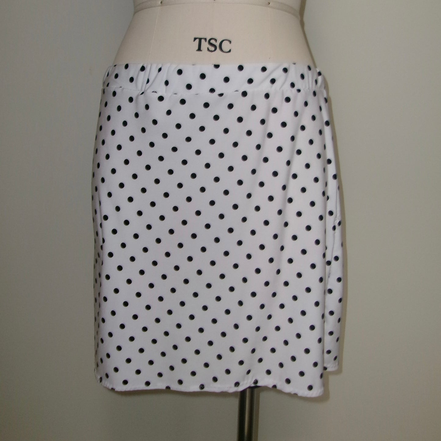 White skirt with black polka dots on a mannequin against a plain background