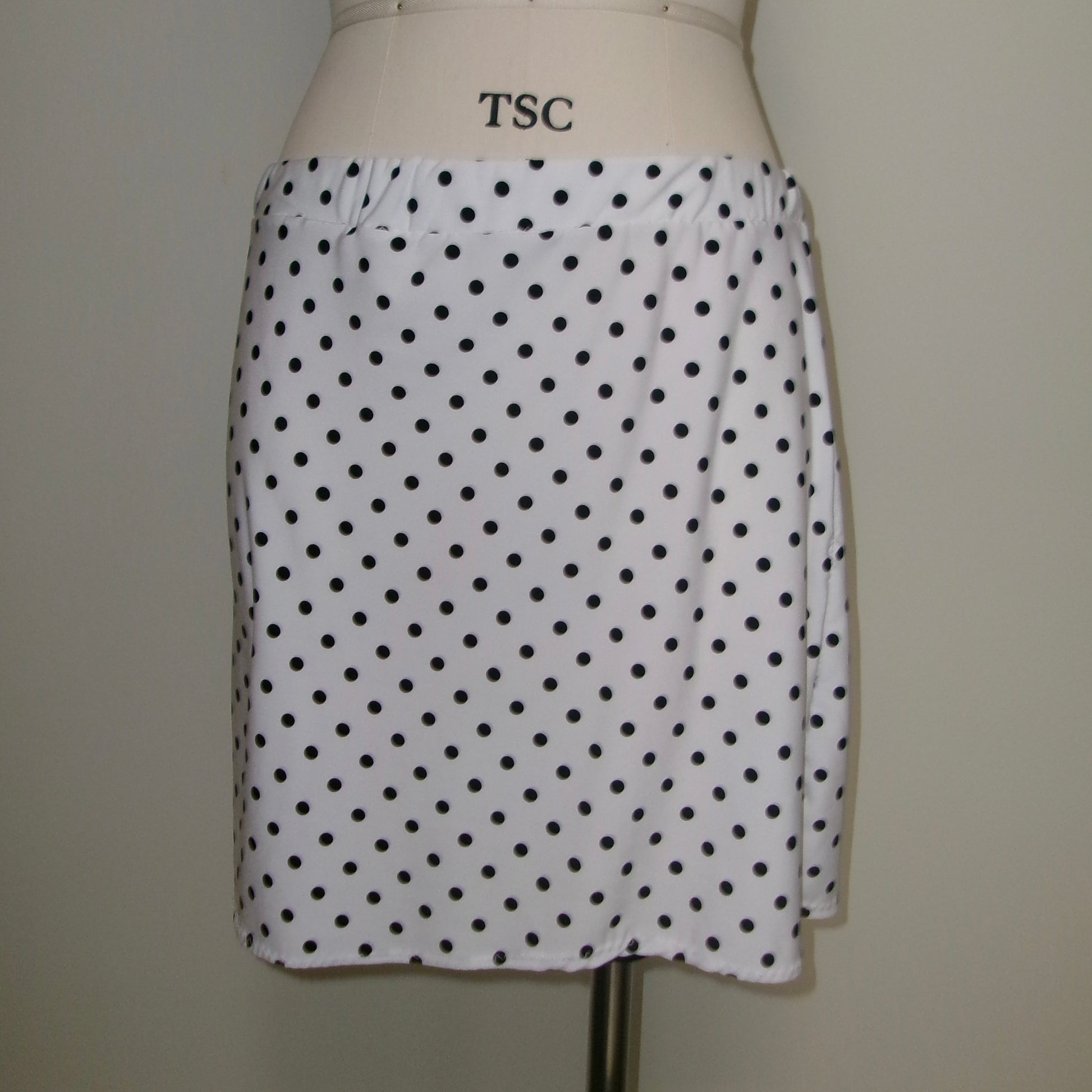 White skirt with black polka dots on a mannequin against a plain background