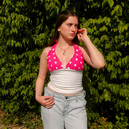 Model wearing a pink and white polka dot halter top with a tie-neck and fitted bodice, standing in natural sunlight.