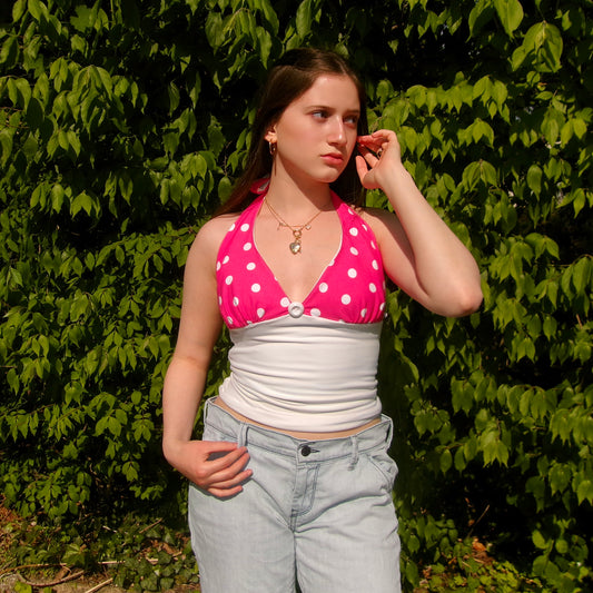Model wearing a pink and white polka dot halter top with a tie-neck and fitted bodice, standing in natural sunlight.