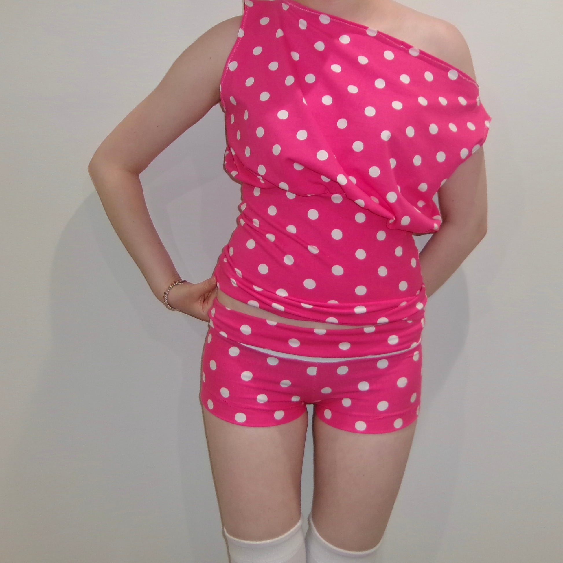 Model wearing a pink and white polka dot off-shoulder tank top. Standing in soft lighting. Retro, trendy, Y2K, preppy, chic