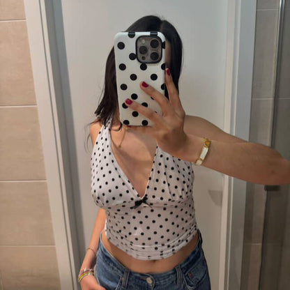 Person taking a mirror selfie wearing a polka dot top and jeans in a bathroom.