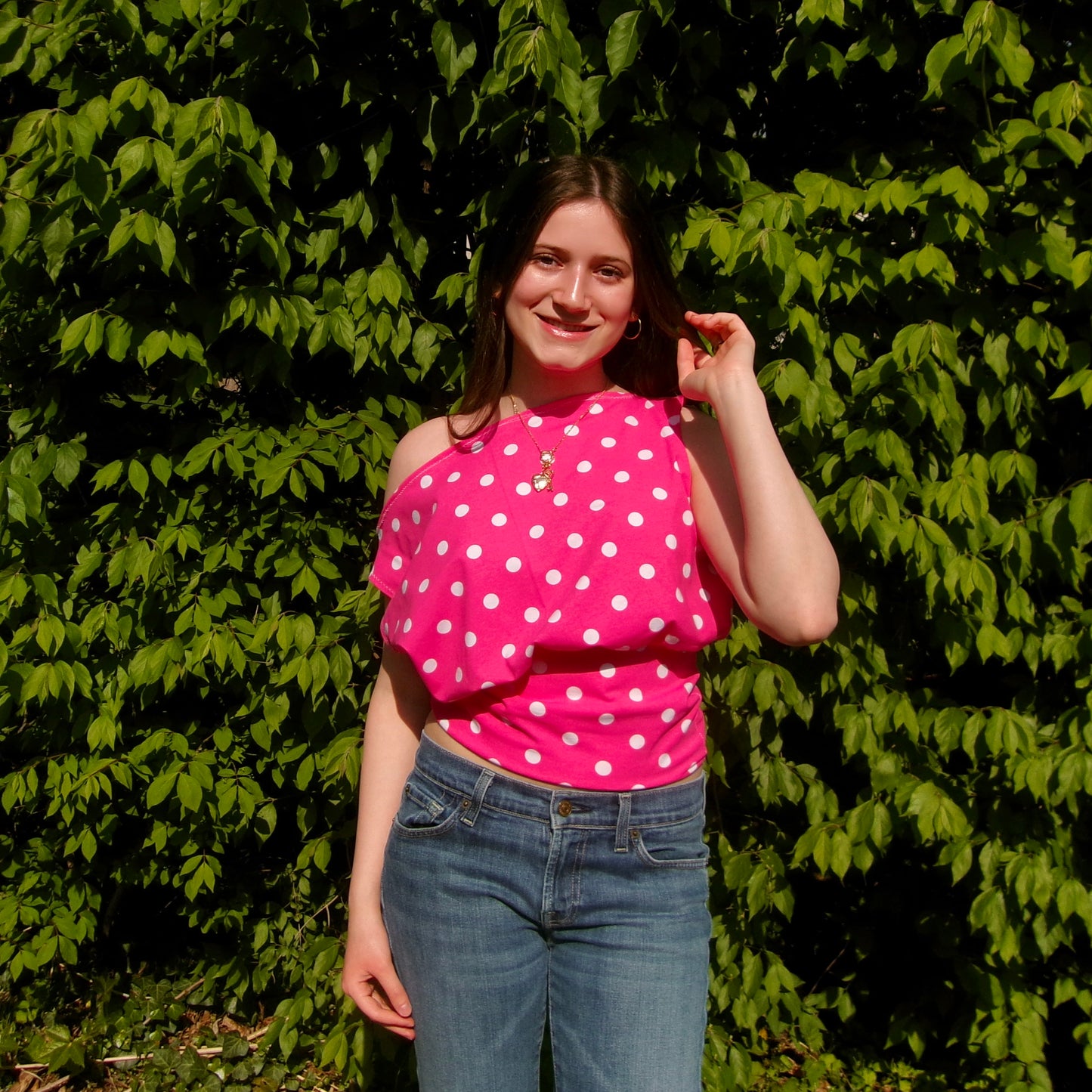 Model wearing a pink and white polka dot off-shoulder tank top. Standing in soft lighting. Retro, trendy, Y2K, preppy, chic