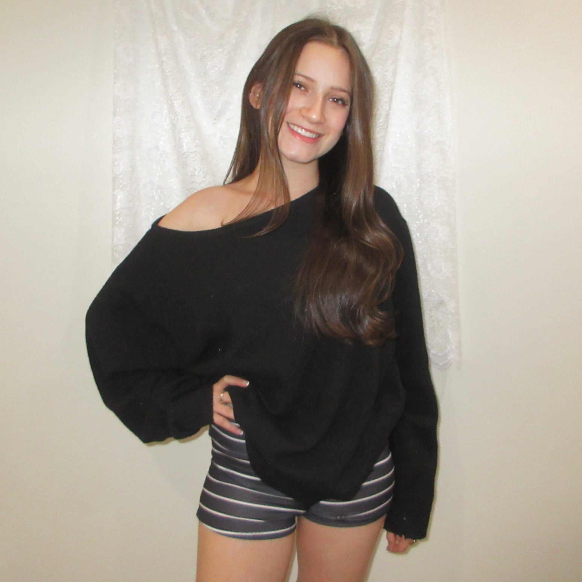 Woman wearing a black sweater and striped shorts against a white curtain background
