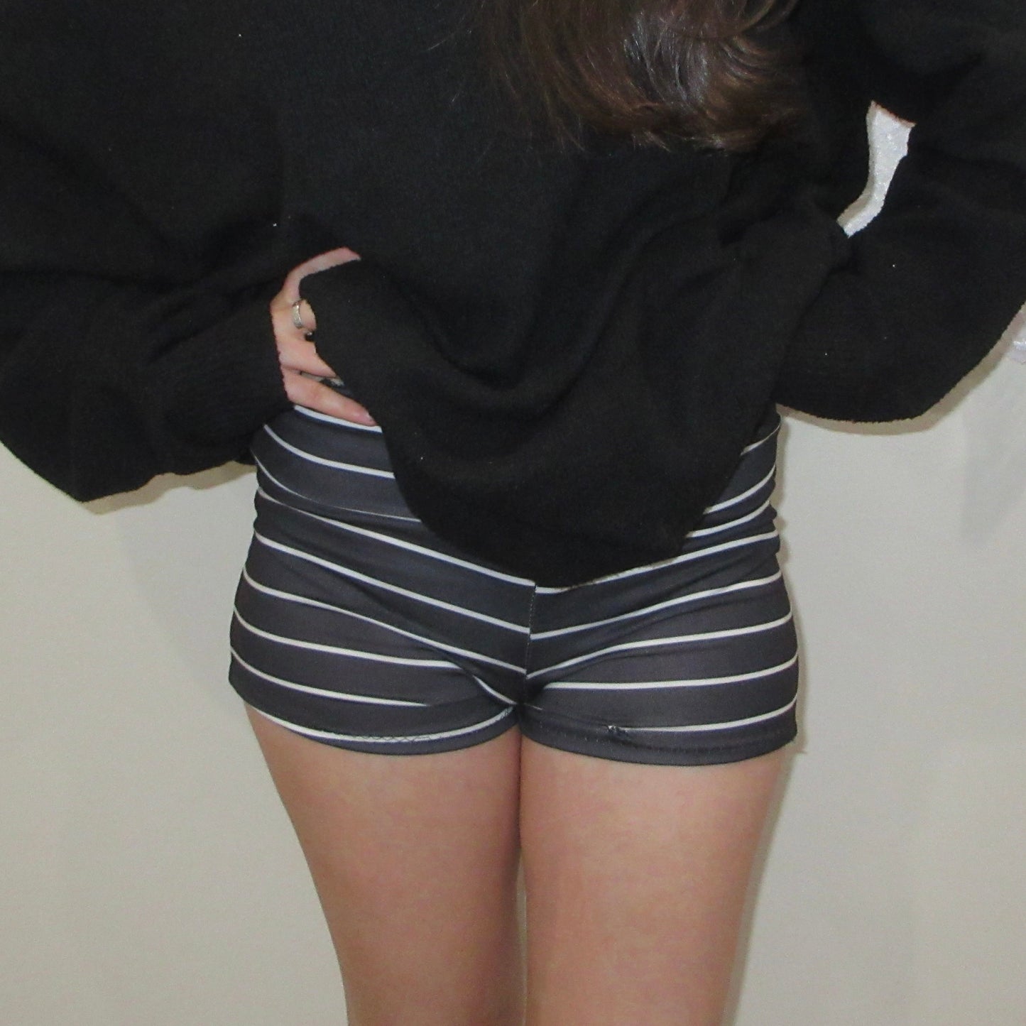 Person wearing a black oversized sweater and striped shorts against a plain background
