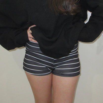 Person wearing a black oversized sweater and striped shorts against a plain background