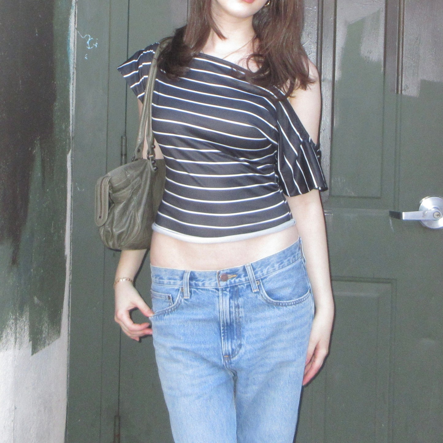 Person wearing a striped top and jeans standing in front of a door.