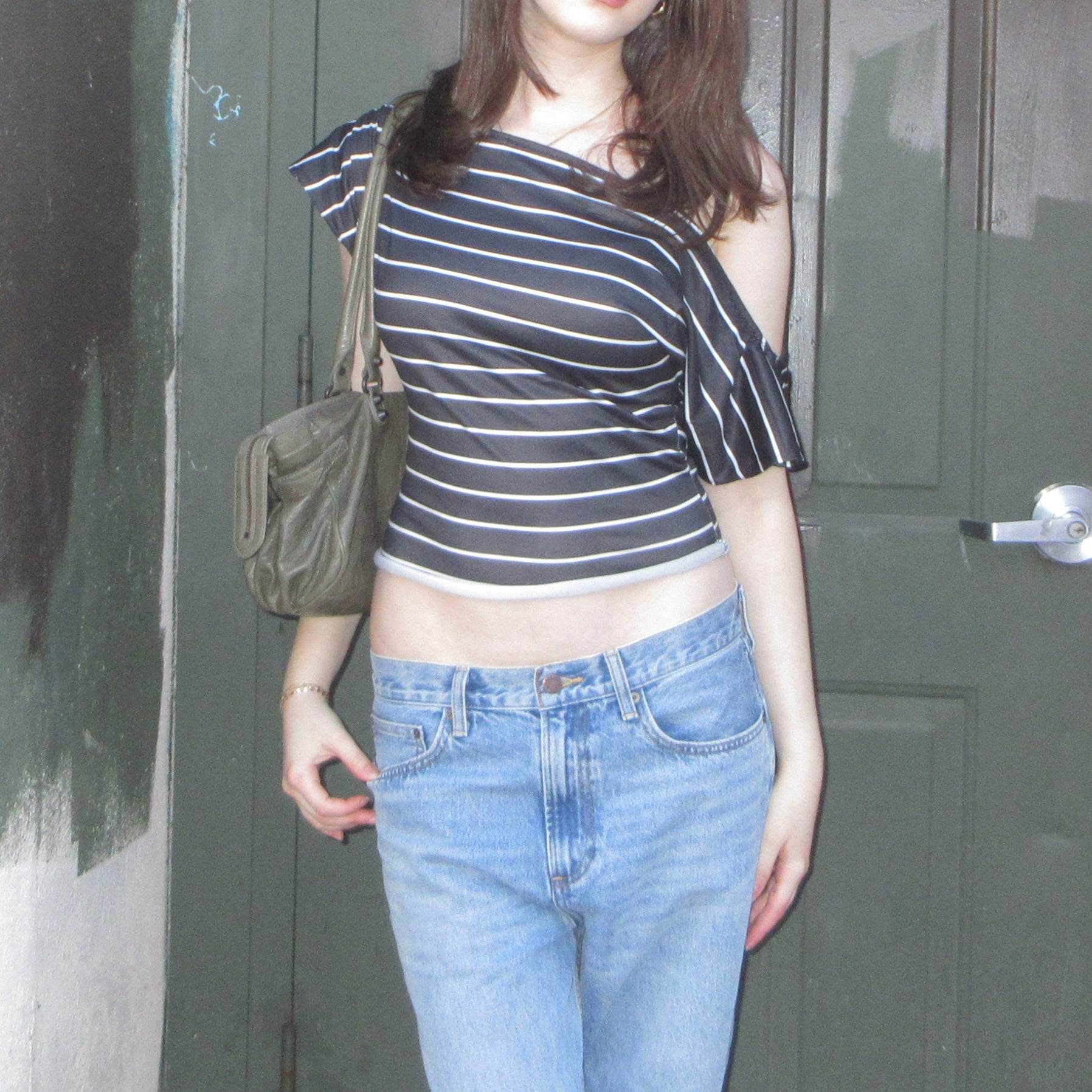 Person wearing a striped top and jeans standing in front of a door.
