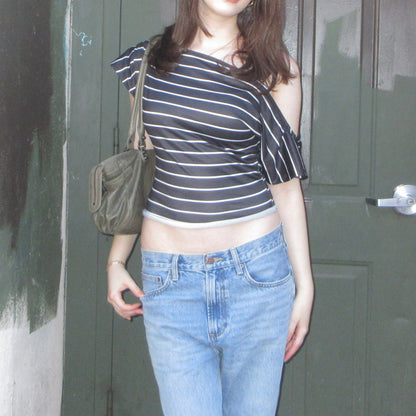 Person wearing a striped top and jeans standing in front of a door.