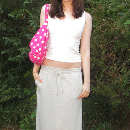 Person wearing a white sleeveless top and gray sweatpants, holding a pink polka dot bag outdoors.