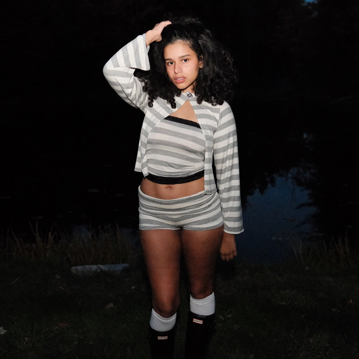 Person wearing a striped outfit standing in a dark forest with a pond.