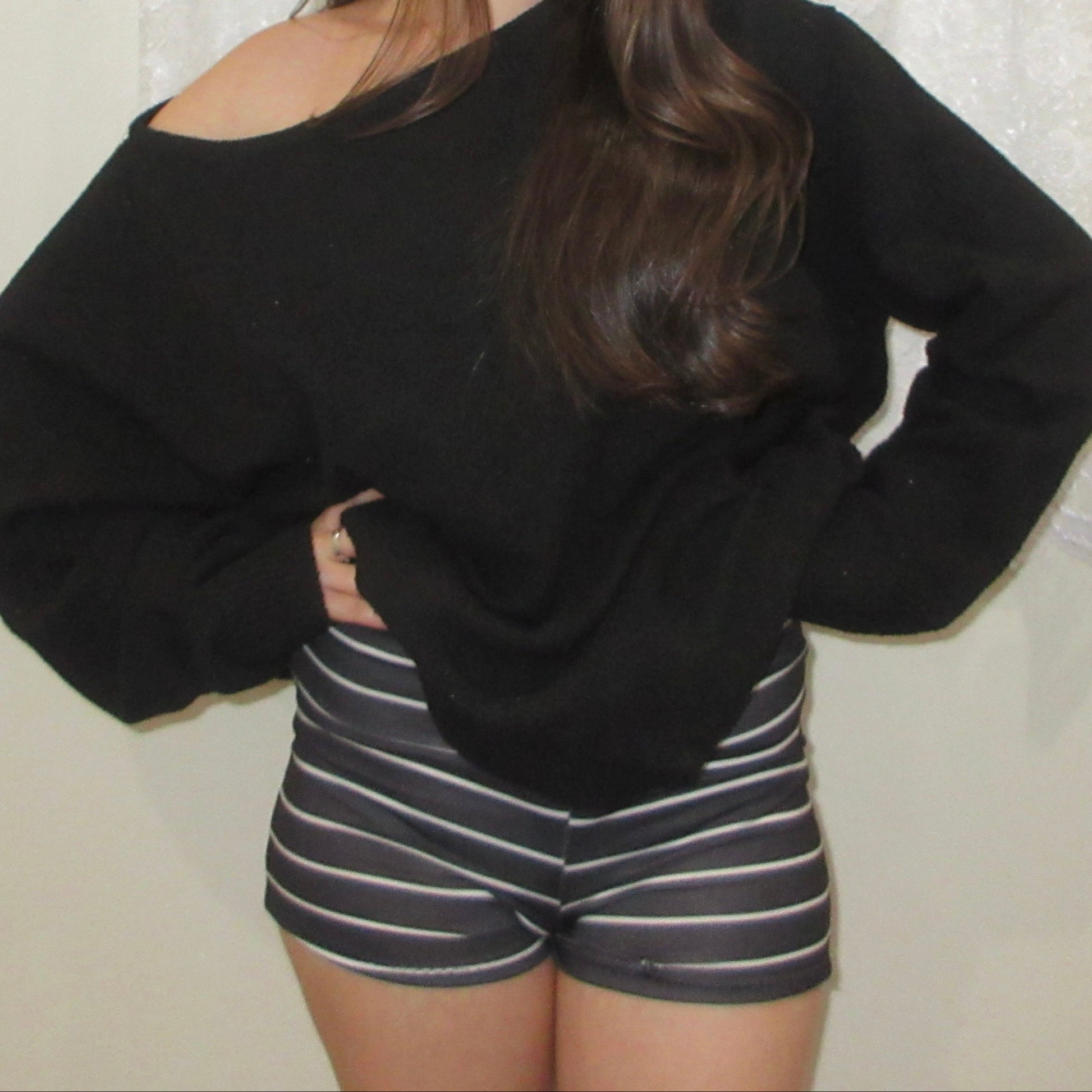 Person wearing a black oversized sweater and striped shorts against a white background