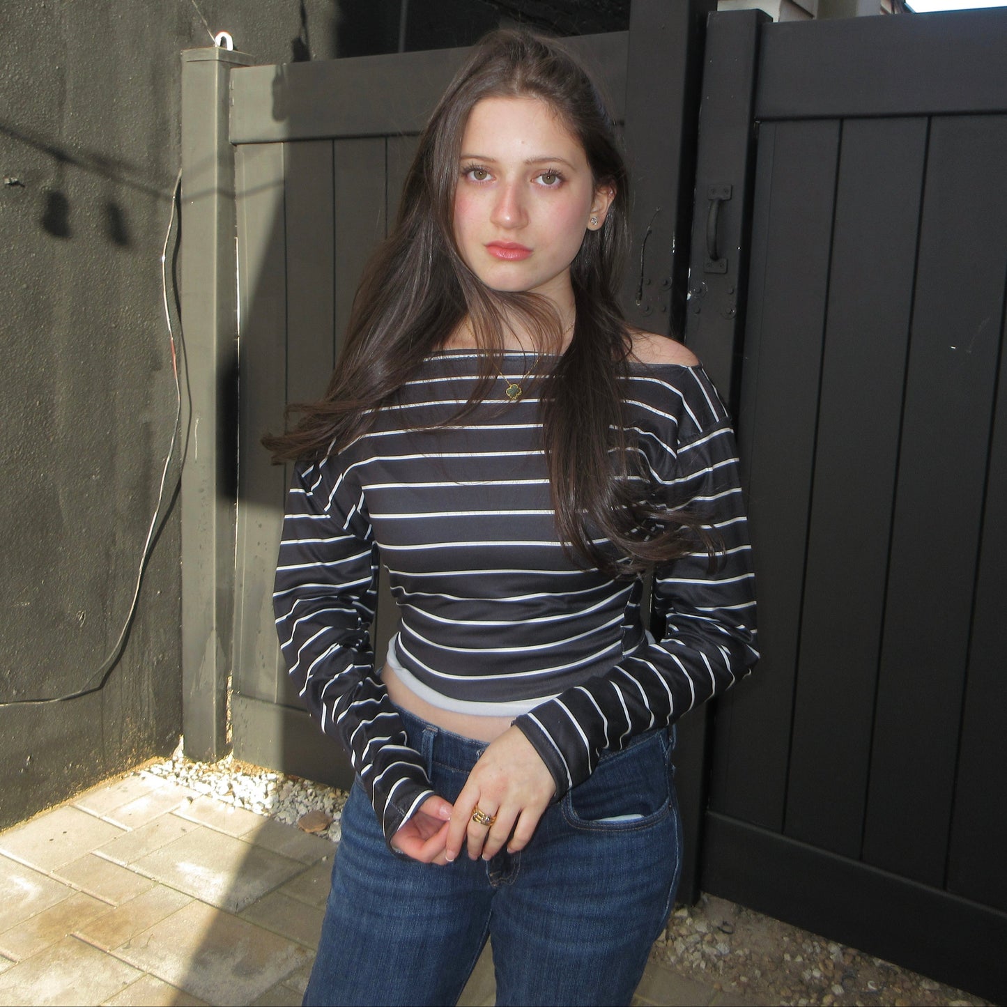 Woman standing in front of a black gate wearing a striped shirt and jeans.