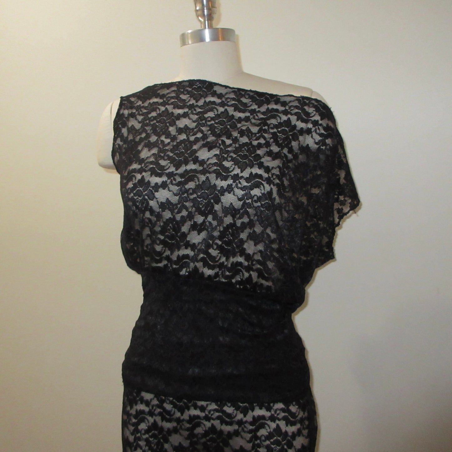 Black lace dress on a mannequin against a plain background
