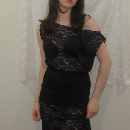 Person wearing a black lace dress against a neutral background