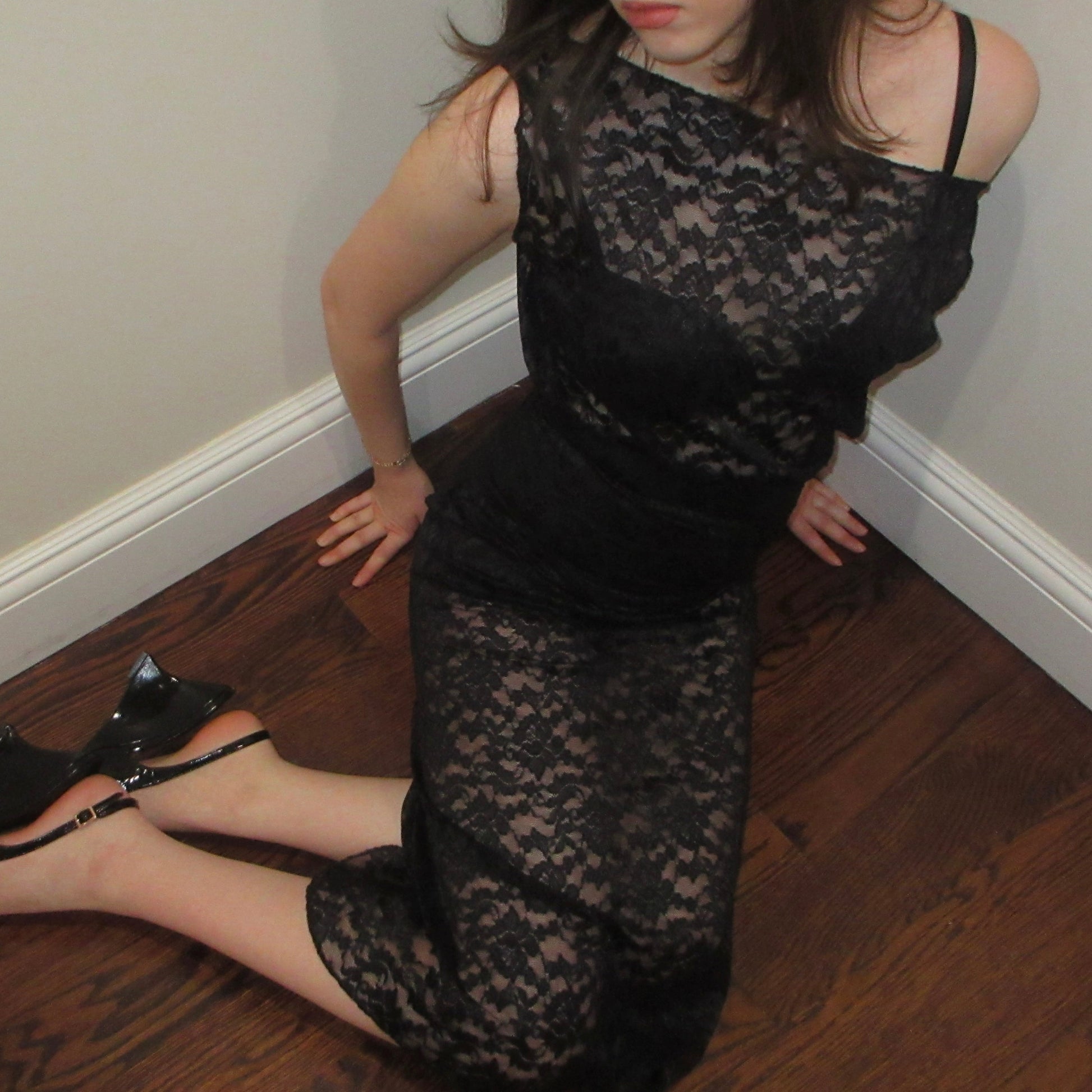 Person wearing a black lace dress and high heels on a wooden floor.