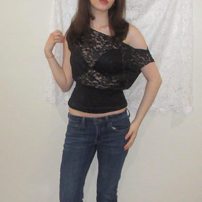 Person wearing a black lace top and blue jeans against a white curtain background