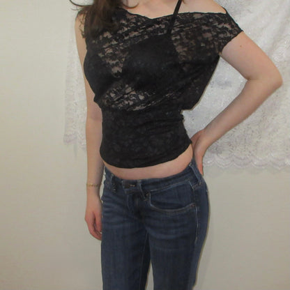 Person wearing a black lace top and blue jeans against a neutral background