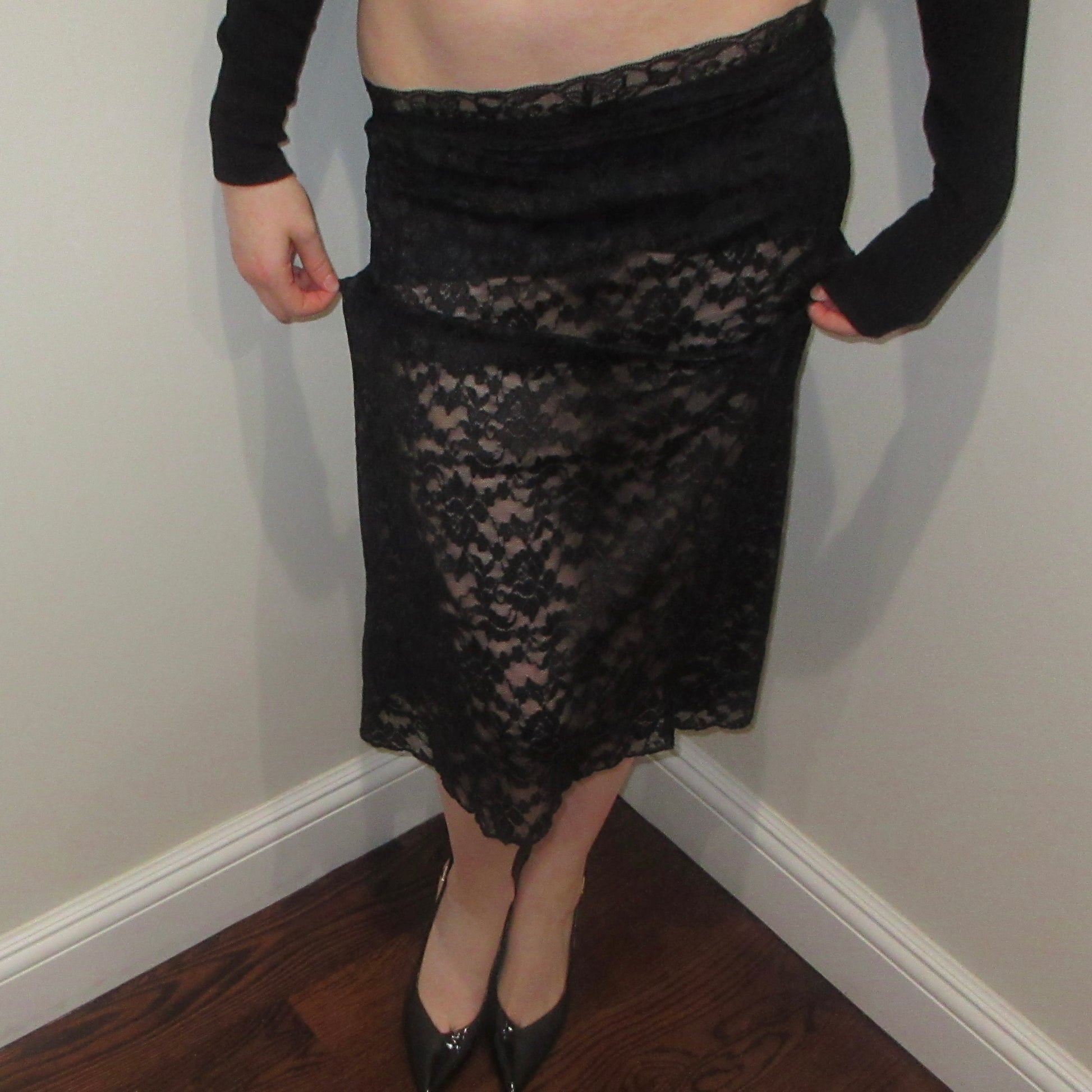 Person wearing a black lace skirt against a plain wall.