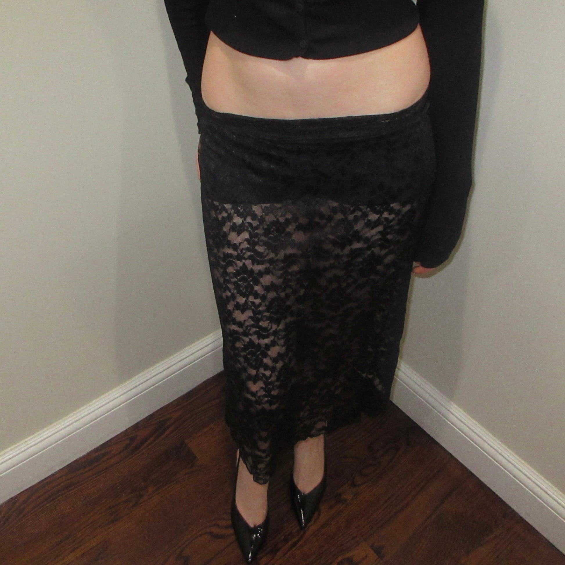 Person wearing a black lace skirt indoors against a plain wall.