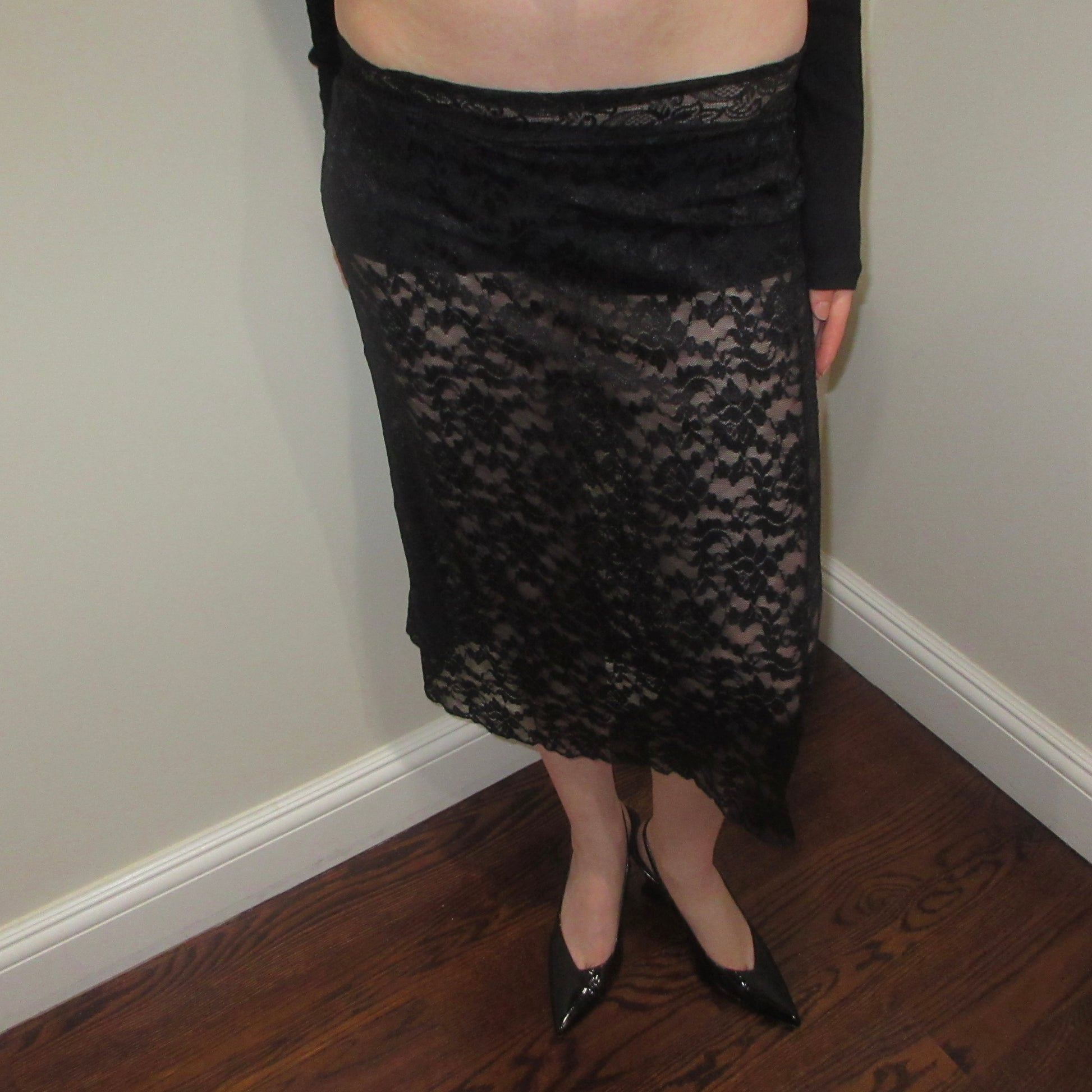 Person wearing a black lace skirt standing against a plain wall.