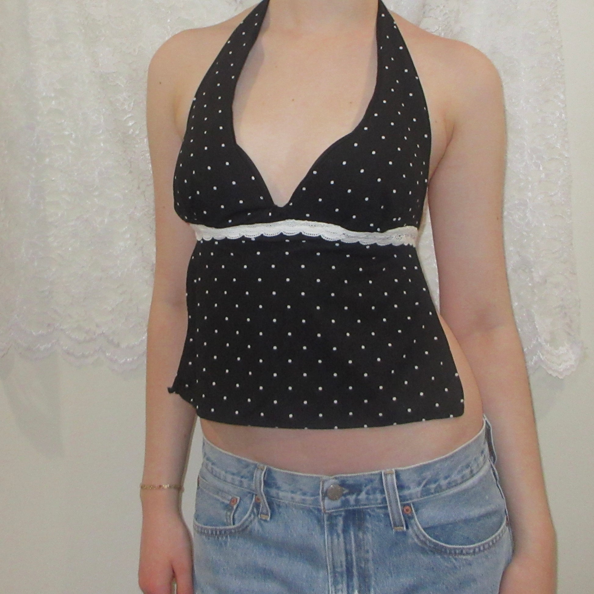 Black polka dot halter top worn by a person with a white lace curtain background