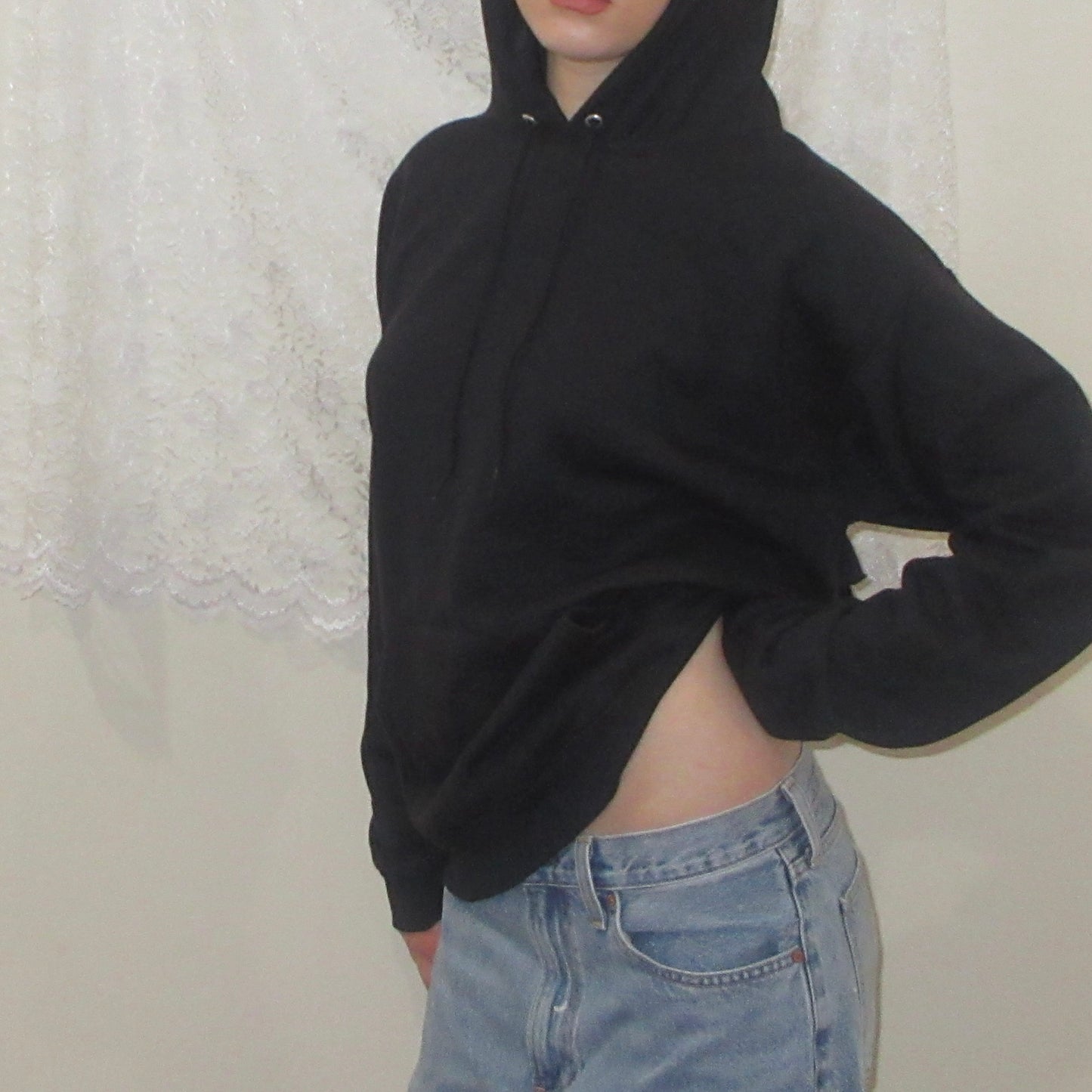 Person wearing a black hoodie and light blue jeans against a neutral background