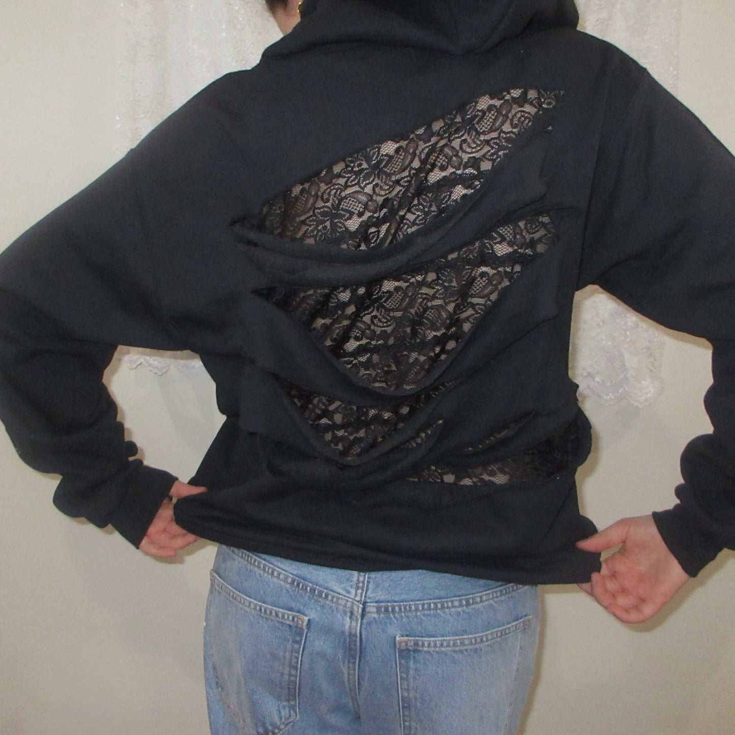 Black hoodie with lace detailing on the back worn by a person against a neutral background