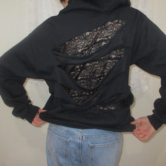Black hoodie with lace detailing on the back worn by a person against a neutral background