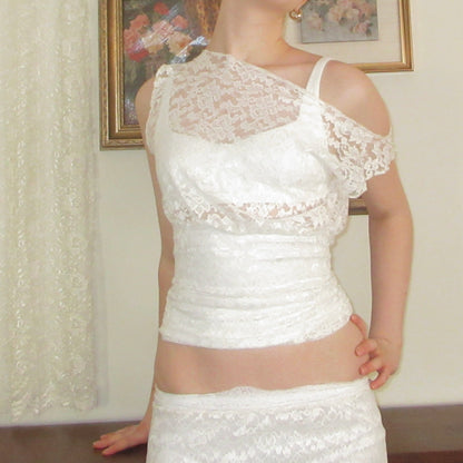 White lace dress worn by a person in a room with framed pictures on the wall.