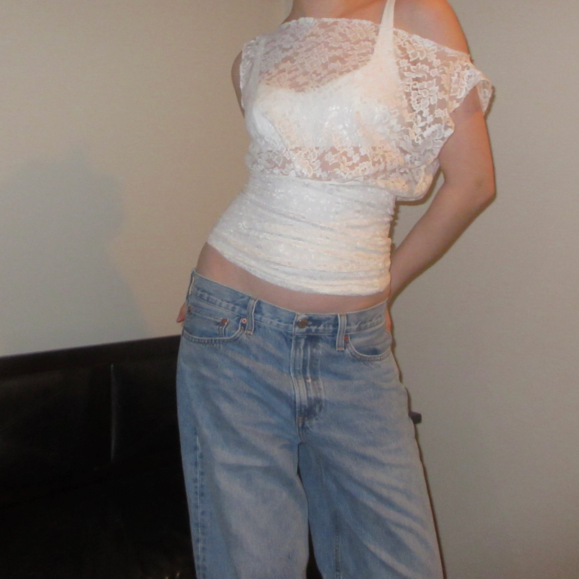 Person wearing a white lace top and blue jeans against a plain background