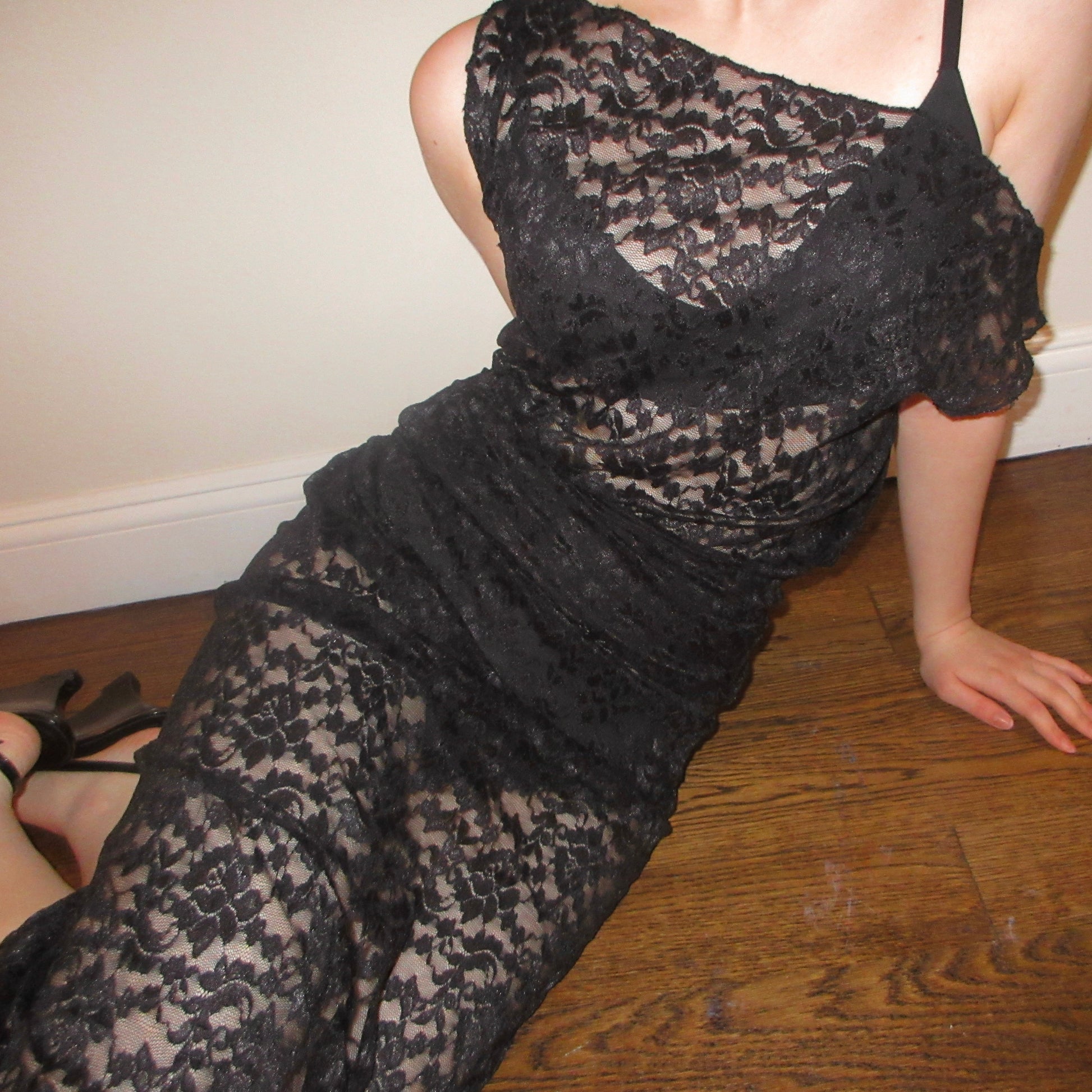 Person wearing a black lace dress on a wooden floor.