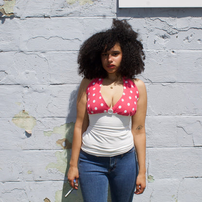 Woman wearing a pink polka dot top over a white shirt against a textured wall.