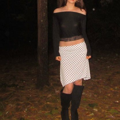 Person wearing a black top and polka dot skirt with knee-high boots in a dark forest setting.