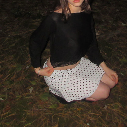 Person wearing a black top and polka dot skirt sitting on the ground.