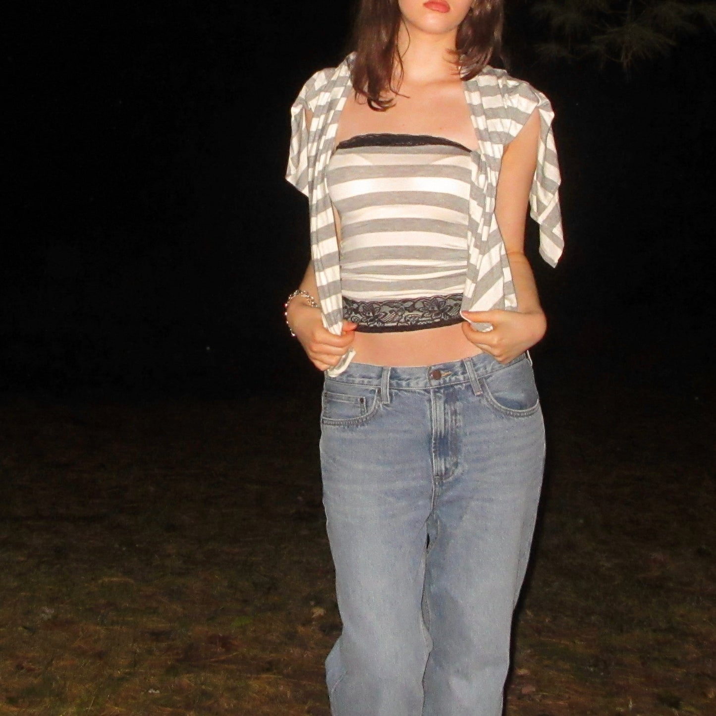 Person wearing a striped crop top and jeans against a dark background