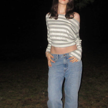 Person wearing a striped crop top and blue jeans standing against a dark background