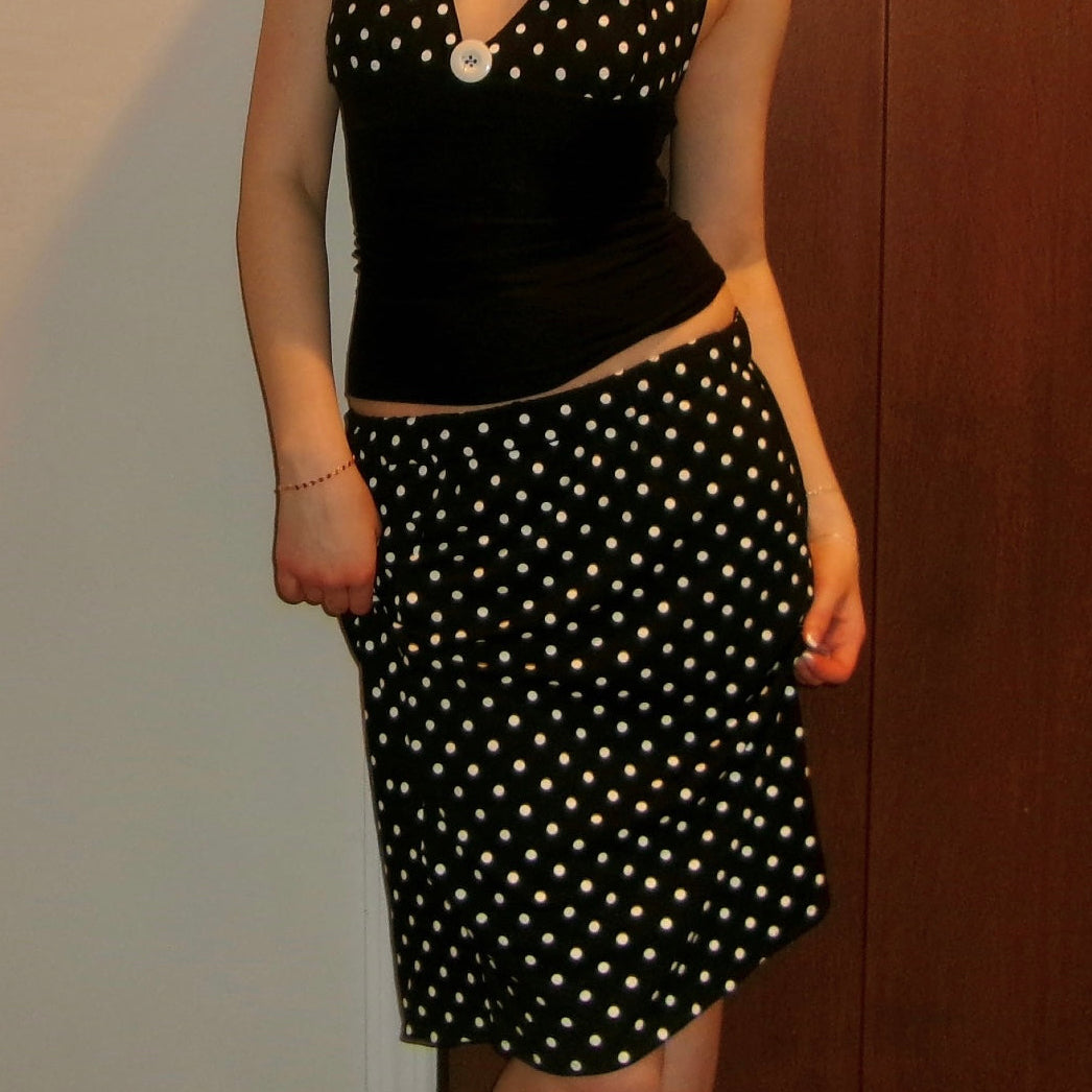 Person wearing a black polka dot top and skirt against a neutral background
